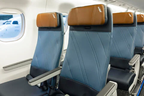 E175 seats with blue upholstery, tan headrests and grey armrests beside a cabin window.