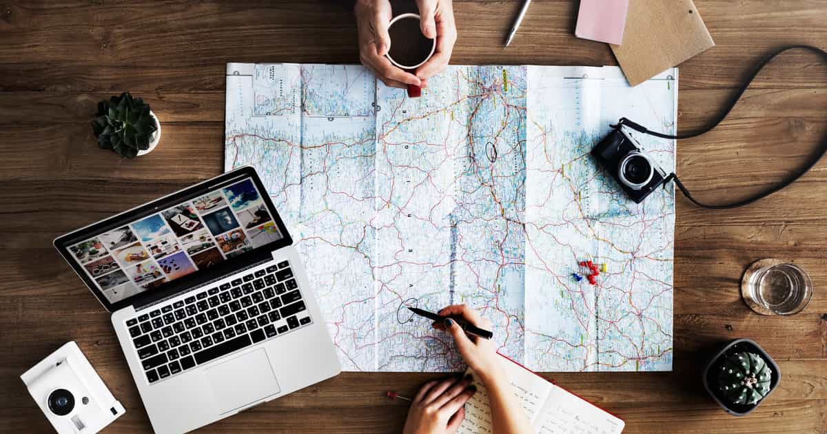 Hands over a paper map beside a laptop, camera and coffee